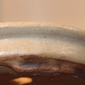 Könnte beinhalten: Nahaufnahme des Rands eines Bonsai-Topfes aus Keramik. Der Topf hat eine hellbraune Glasur mit einem dunkleren braunen Rand.