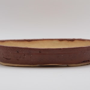 Op de afbeelding: Een bruine, ovale keramische bonsai pot met een getextureerde buitenkant en een lichtbeige binnenkant. De pot is ongeveer 25 cm lang en 15 cm breed, geschikt voor kleine planten of bonsai bomen.