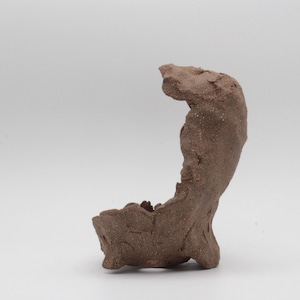 May include: A handcrafted, brown ceramic sculpture with a unique, organic shape. The piece features a textured surface and an open, bowl-like form at the base, rising into a curved, abstract design. The sculpture is suitable for home decor.