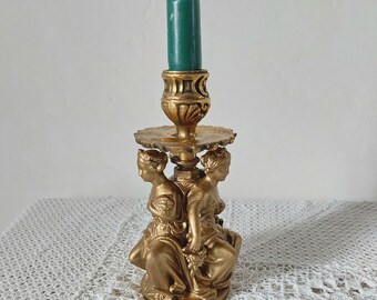 May include: Gold candlestick with three figures holding up a candle holder. The candle is green.