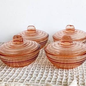 Op de afbeelding: Set van vier vintage roze glazen schalen met deksel en een swirl-ontwerp. De schalen zijn perfect om snacks of desserts te serveren.