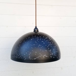 Puede incluir: Una lámpara colgante de forma de cúpula negra con un patrón de constelación blanca. La luz cuelga de un cordón marrón.
