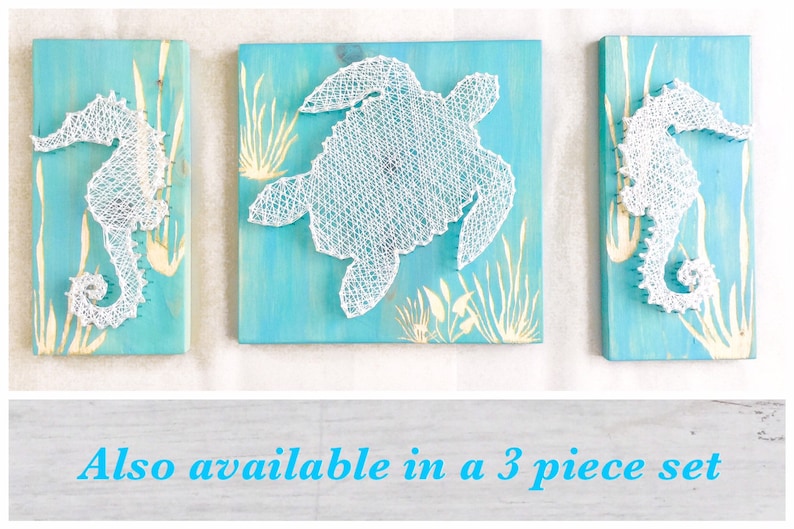 May include: Three string art pieces on a blue background. The center piece is a white turtle, and the pieces on either side are white seahorses. The text "Also available in a 3 piece set" is below the images.