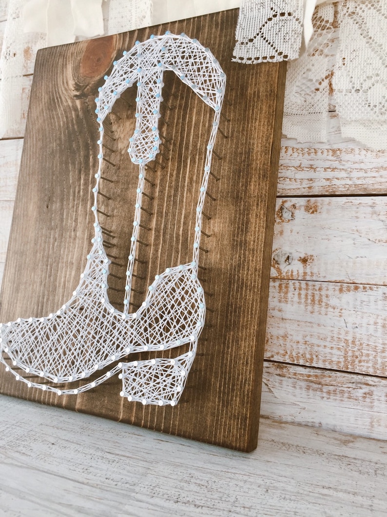 Puede incluir: Arte de hilo blanco de una bota vaquera sobre un fondo de madera marr&oacute;n oscuro. La bota est&aacute; delineada con hilo blanco y los detalles est&aacute;n rellenos con hilo blanco.