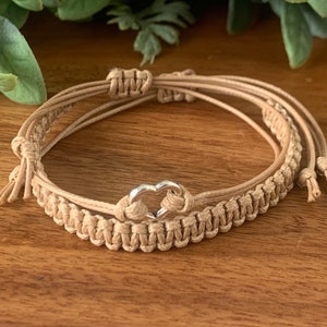May include: A tan braided friendship bracelet with a silver heart charm.