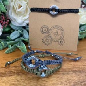 Könnte beinhalten: Zwei Freundschaftsarmbänder mit Metallmuttern als Mittelstücke. Ein Armband ist grau und das andere grün.