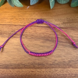 May include: A purple and pink friendship bracelet with a knotted design.