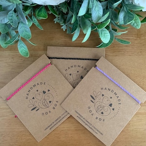 Può includere: Tre braccialetti fatti a mano con cordini rosa, neri e viola sono presentati su biglietti marroni. Ogni biglietto presenta un design circolare con le parole "HANDMADE FOR YOU" e il testo "HANDMADE IN CANNOCK, STAFFORDSHIRE wishfulthinkingbyfay@etsy.com".