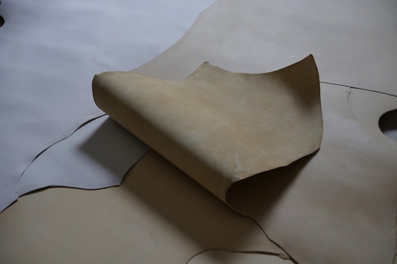 May include: Two pieces of light brown leather, one folded over the other. The leather is smooth and has a natural, slightly textured surface.