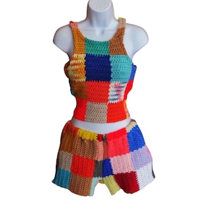 May include: A colorful, patchwork crochet top and shorts set. The top is a tank style, and the shorts are high-waisted. The set features squares of red, orange, blue, green, and tan. The outfit is displayed on a white mannequin.