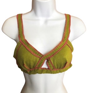 May include: Olive green knitted bra with a contrasting coral trim. The bra features a V-neck design with a keyhole detail at the center. The straps and edges are outlined with the coral trim.