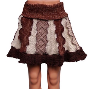 May include: A brown and cream-colored knitted skirt with a unique design. The skirt features a high, ribbed waistband and a flared hem. The skirt has a mix of textures, including cable knit and wavy patterns. The skirt is displayed on a mannequin.