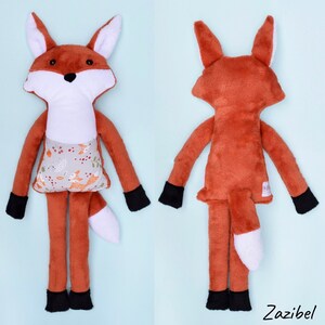 May include: A handmade plush fox toy with a white belly and a brown and white tail. The fox is wearing a gray and white fabric with a pattern of foxes and berries. The toy is standing on a light blue background.