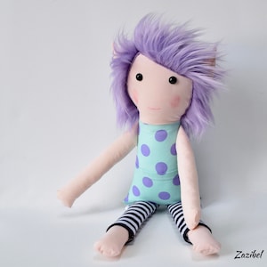 Peut inclure: Une poupée faite à la main avec des cheveux en fourrure violette, une robe à pois turquoise et violet et un legging rayé noir et blanc.