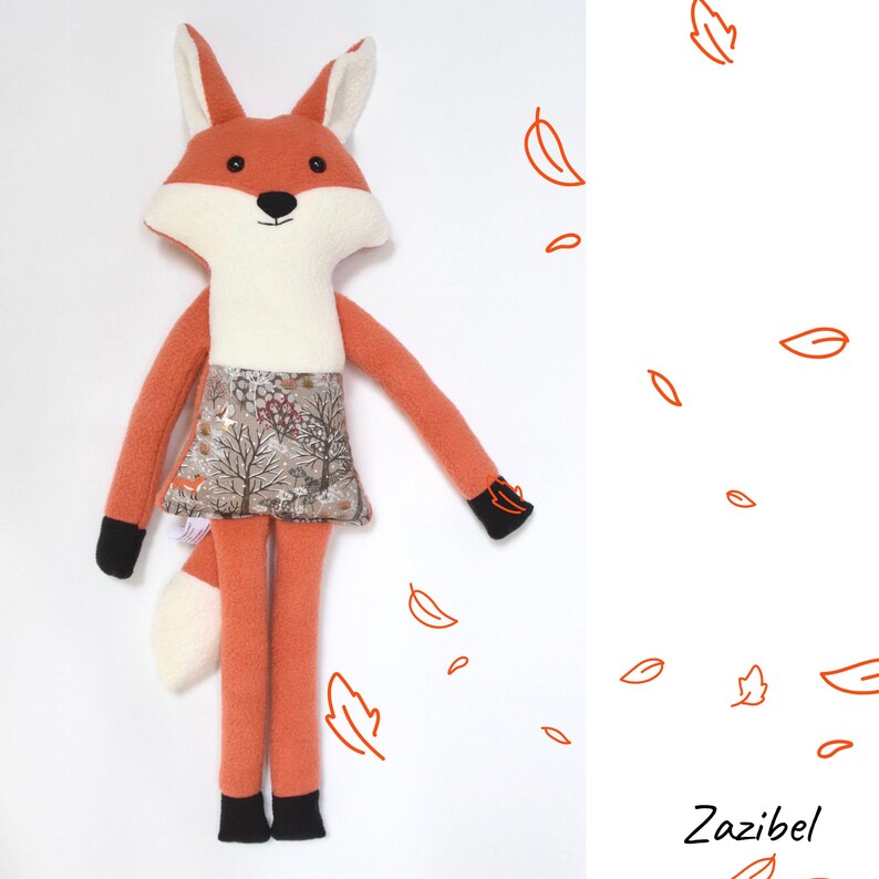 May include: A handmade orange fox plush toy with a white belly and a brown and white patterned skirt. The fox is standing on a white background with orange leaf drawings.