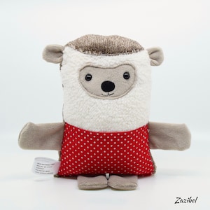 May include: A plush toy shaped like a sheep with a red and white polka dot skirt. The toy has a brown head and a white body. The toy has a friendly face with black eyes and a black nose.
