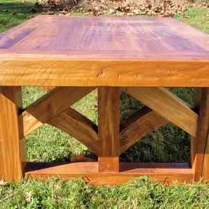 May include: A rustic wooden coffee table with a rectangular top and a geometric, open-frame base. The table is made of natural wood with a rich brown color and a distressed finish.