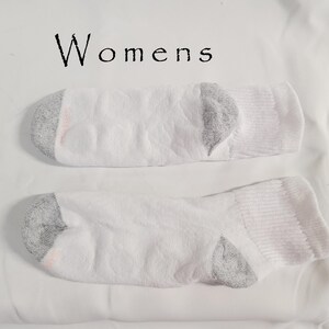 Pu&ograve; includere: Un paio di calzini bianchi con talloni e punte grigie rinforzate. I calzini presentano un sottile motivo circolare testurizzato su tutto il tessuto. La parola "Womens" &egrave; stampata in nero sopra i calzini, dotati di polsini a coste.