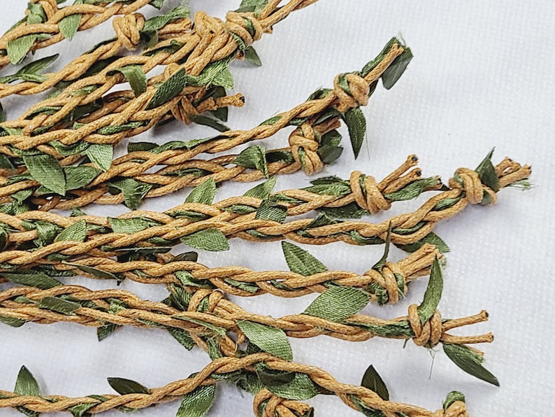 May include: A collection of tan twine strands braided with thin green fabric leaves. Each strand features a series of small knots spaced along the length, creating a textured, vine-like appearance with a natural color palette of brown and green.