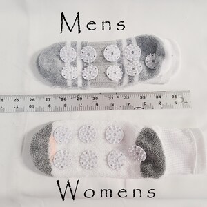 Pu&ograve; includere: Due calzini con dischi di agopressione in plastica bianca sulle suole, etichettati Mens e Womens. Un righello &egrave; posizionato tra loro, mostrando una lunghezza di circa 33 cm per il calzino superiore e 28 cm per quello inferiore.