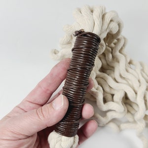 May include: A white cotton rope with a brown leather handle. The handle is wrapped tightly with leather and has a natural, rustic look.