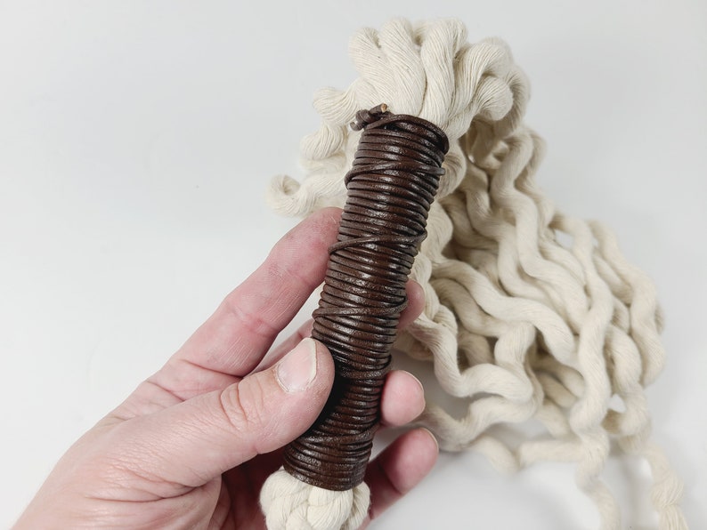May include: A white cotton rope with a brown leather handle. The handle is wrapped tightly with leather and has a natural, rustic look.