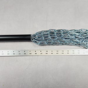 Puede incluir: Un mango de metal negro con un mayal de cadena plateada. La cadena est&aacute; hecha de eslabones de metal entrelazados. Se coloca una regla junto al mayal para mostrar la longitud del objeto.