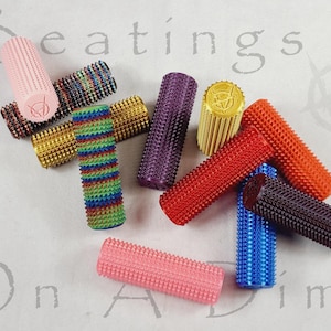 May include: A collection of colorful, textured cylindrical objects. The objects are in various colors, including pink, red, blue, purple, and gold. Some have a spiked texture, while others have a smooth, ridged surface. The word "Beatings" is visible in the background.