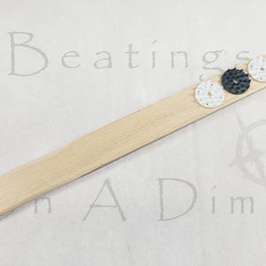 May include: A light-colored wooden incense holder with three small, round incense holders. Two are white with a floral design, and one is black with a textured surface. The text "Beatings A Dime" is faintly visible.
