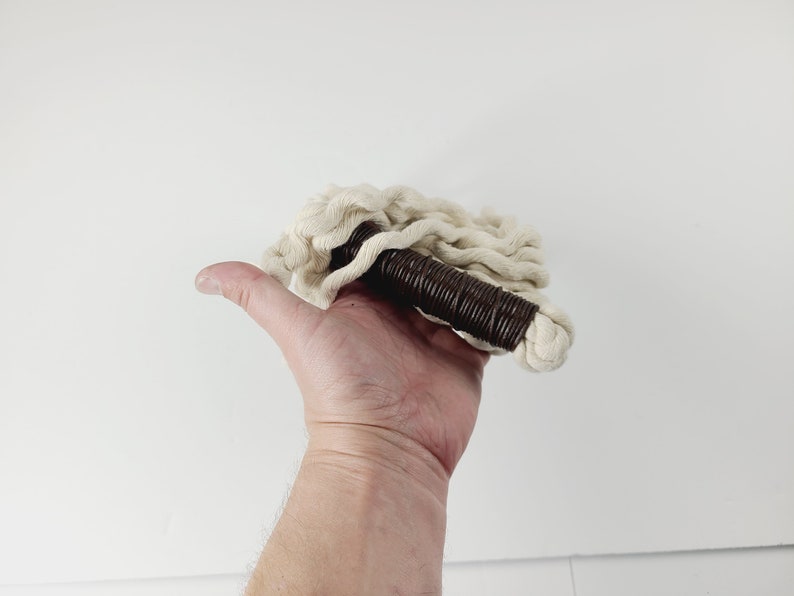 May include: A white cotton rope with a brown handle. The rope is coiled and the handle is made of a brown material.