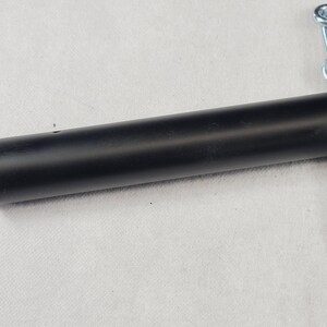 Puede incluir: Un mango cil&iacute;ndrico negro de metal con una cadena plateada adjunta. El mango es liso y tiene un peque&ntilde;o agujero cerca del centro. La cadena est&aacute; hecha de eslabones met&aacute;licos entrelazados.