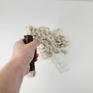 May include: A white cotton rope whip with a brown handle. The whip is coiled and ready to be used.