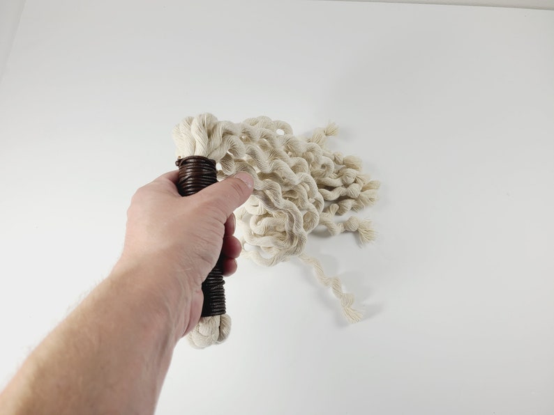 May include: A white cotton rope whip with a brown handle. The whip is coiled and ready to be used.