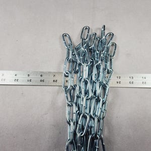 Puede incluir: Un conjunto de eslabones de cadena de metal plateado junto a una regla. La regla muestra medidas en pulgadas, con marcas de 1 a 34. La cadena est&aacute; hecha de eslabones ovalados entrelazados.