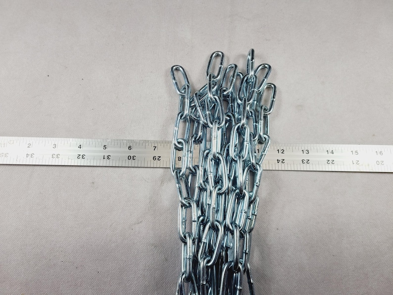 Puede incluir: Un conjunto de eslabones de cadena de metal plateado junto a una regla. La regla muestra medidas en pulgadas, con marcas de 1 a 34. La cadena est&aacute; hecha de eslabones ovalados entrelazados.