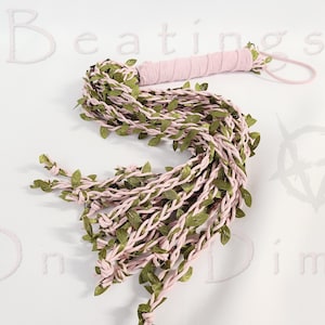May include: A light pink braided whip featuring a wrapped handle and a wrist loop, adorned with numerous small green fabric leaves woven throughout the length of the strands. The text Beatings On a Dime is visible in the background.