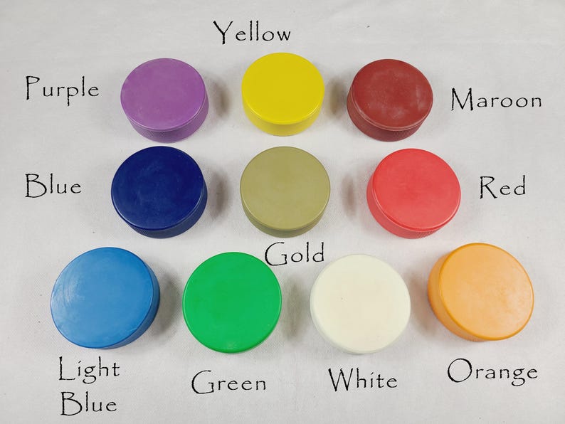 May include: Ten small, round, lidded containers in a variety of colours are displayed. The colours include purple, yellow, maroon, blue, gold, red, light blue, green, white, and orange. Each colour is labelled with handwritten text.