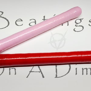 Könnte beinhalten: Zwei zylindrische Objekte, eines rosa und eines roten, liegen diagonal auf einer weißen Oberfläche. Das rosa Objekt befindet sich über dem roten. Die Worte "Beatings On A Dime" sind grau auf der Oberfläche gedruckt.