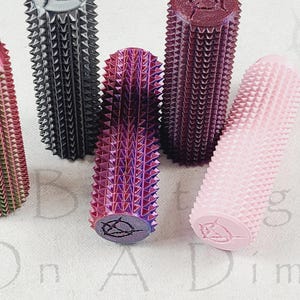 May include: A collection of textured, cylindrical objects in various colors, including green, black, purple, and pink. Each object has a spiked surface and a rounded top. The objects are arranged on a white surface.