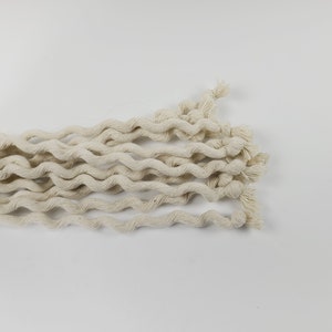 May include: A close-up of a bundle of natural white cotton rope, twisted and coiled together. The rope is soft and textured, with a slightly rough surface.