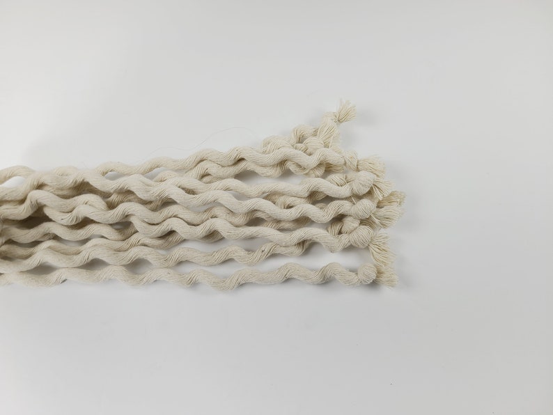 May include: A close-up of a bundle of natural white cotton rope, twisted and coiled together. The rope is soft and textured, with a slightly rough surface.