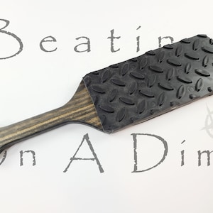 May include: A black paddle with a textured surface and a wooden handle. The paddle is made of rubber and has a diamond pattern.