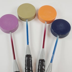 May include: Four bottle stoppers in various colours. Each stopper features a circular, solid-coloured top and a long, thin handle. The handles transition from a dark hue to a lighter shade. The stoppers have black grips.