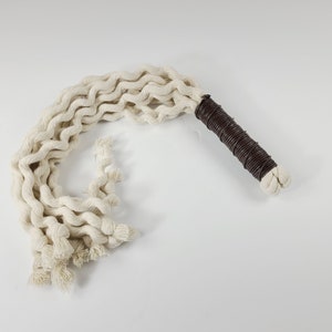 May include: A white cotton rope whip with a brown leather handle. The rope is braided and has a fringed end.