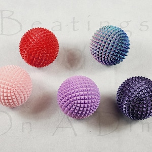 May include: Six colourful, spiky spheres in red, pink, purple, blue, and a blue-purple gradient. The spheres have a textured, geometric surface and are arranged on a white background.