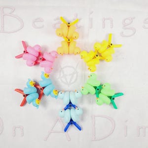 May include: A colorful set of rubber duck toys arranged in a star shape on a white background. The ducks are in various colors, including pink, blue, green, and yellow. The text "Beatings On A Dime" is written in pink on the white background.