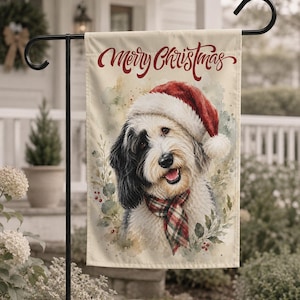 May include: A rectangular garden flag featuring a watercolor illustration of a black and white dog wearing a red Santa hat and a red and green plaid scarf. The text Merry Christmas is printed in red script at the top, surrounded by greenery.