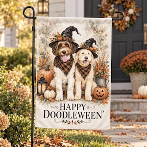May include: A rectangular garden flag featuring two dogs wearing black witch hats and orange and black plaid bandanas. The scene includes pumpkins, a lantern, and autumn foliage. The text reads Happy Doodleween in black lettering.