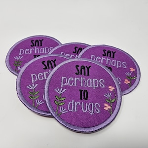 May include: Five purple felt patches with embroidered text that reads "SAY perhaps TO drugs". Each patch has a circular shape with a purple border and floral embroidery. The patches are arranged in a slightly overlapping pattern.