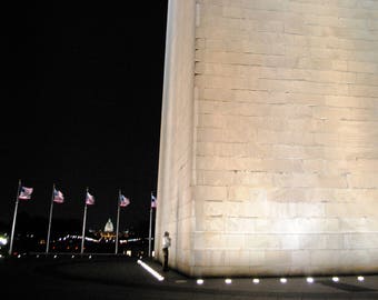 May include: A night view of the Washington Monument in Washington, D.C. The monument is made of white stone and is illuminated by lights. There are American flags flying in the background.